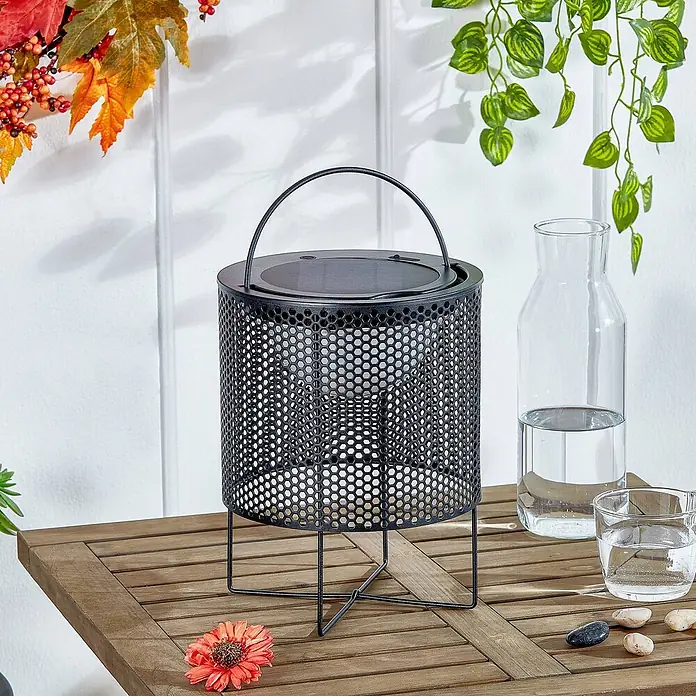 Lindby Tischleuchte Achilleas - L x B x H: 20 x 20 x 26 cm, schwarz - Schwarze perforierte Metall-Solarlaterne mit Griff auf einem Holztisch.