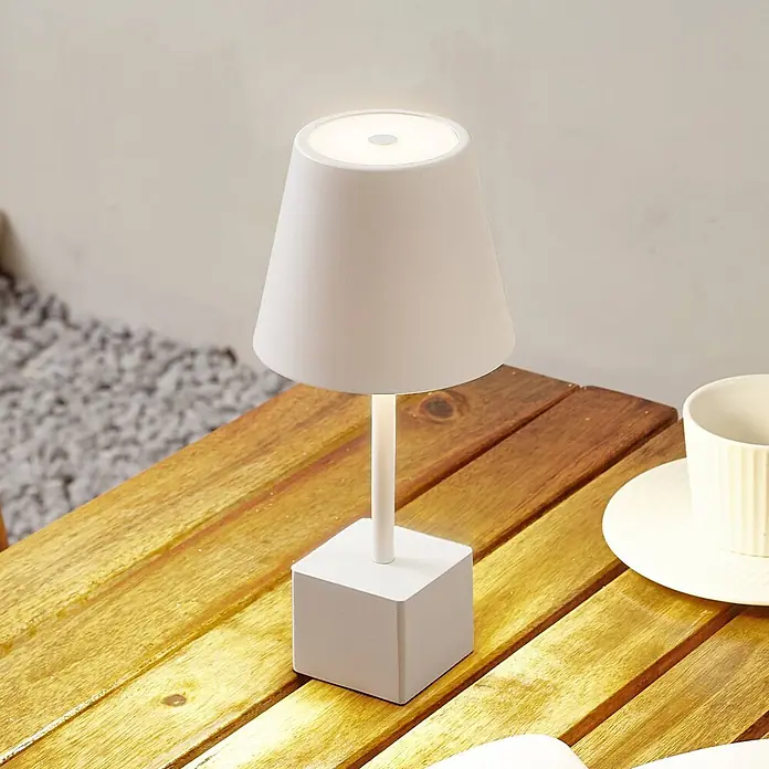 Lindby Tischleuchte Janea - weiß / opal, weiß / opal - Eine minimalistische weiße Tischlampe mit quadratischem Fuß beleuchtet einen hölzernen Lattenrosttisch.