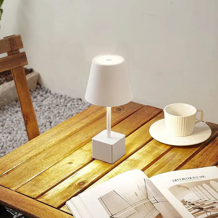 Lindby Tischleuchte Janea - weiß / opal, weiß / opal - Weiße kabellose Tischlampe mit konischem Schirm und quadratischem Sockel auf einem Holztisch im Freien, beleuchtet.
