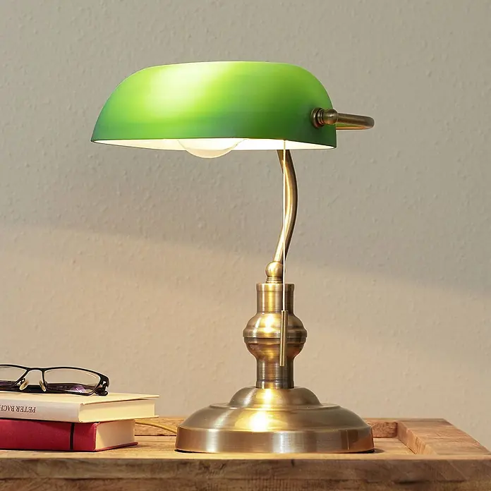 Lindby Tischleuchte Milenka - L x B x H: 18,5 x 23 x 38 cm, bronze / altmessing, grün, E27 - Klassische Bankierlampe mit grünem Glasschirm und messingfarbenem Fuß auf Holztisch neben Büchern und Brille.