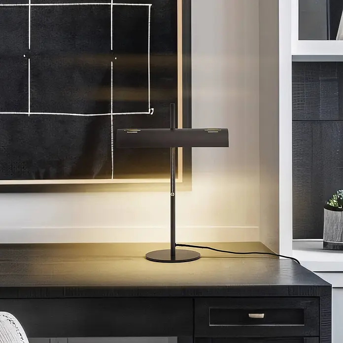 Lucande Tischleuchte Nysira - L x B x H: 18 x 36 x 50 cm, schwarz, schwarz, E27 - Eine schwarze Schreibtischlampe mit rechteckigem Kopf und dezenten Messingakzenten beleuchtet einen dunklen Holzschreibtisch, modernes Design.