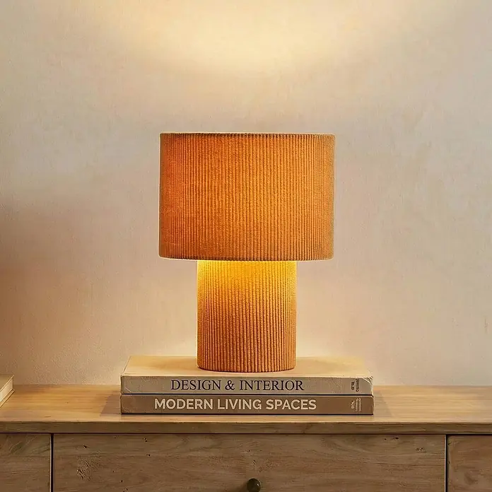 Lindby Tischleuchte Jone - braun / rost, braun / rost, E27 - Beleuchtete orange gerippte Tischlampe auf einem Holztisch mit Büchern.