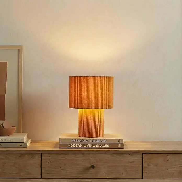 Lindby Tischleuchte Jone - braun / rost, braun / rost, E27 - Gerippte Terrakotta-Tischlampe, leuchtend, auf einer Holzkommode mit Büchern. Ihr warmes Licht erhellt die Wand.