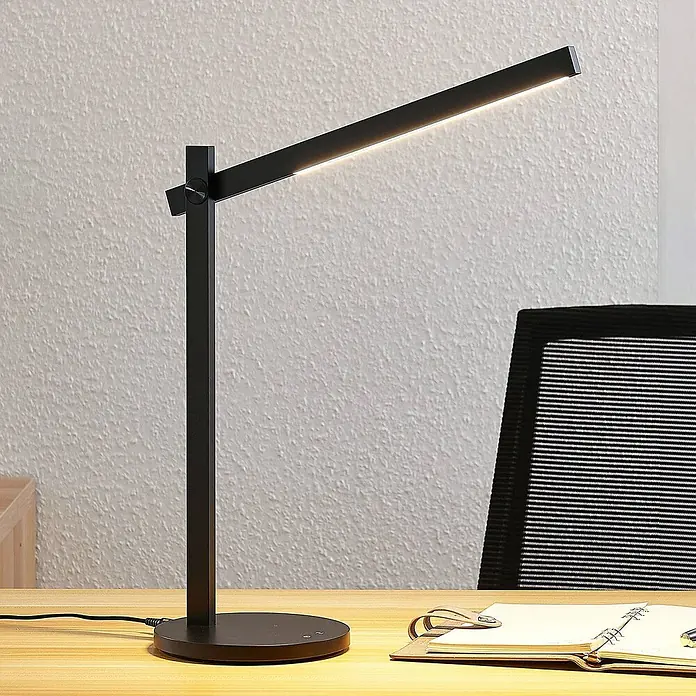 Lindby Tischleuchte Loretta - L x B x H: 40,8 x 17 x 43 cm, schwarz, schwarz - Schwarze, moderne LED-Schreibtischlampe mit verstellbarem Arm, beleuchtet einen Arbeitsbereich auf einem Holzschreibtisch.