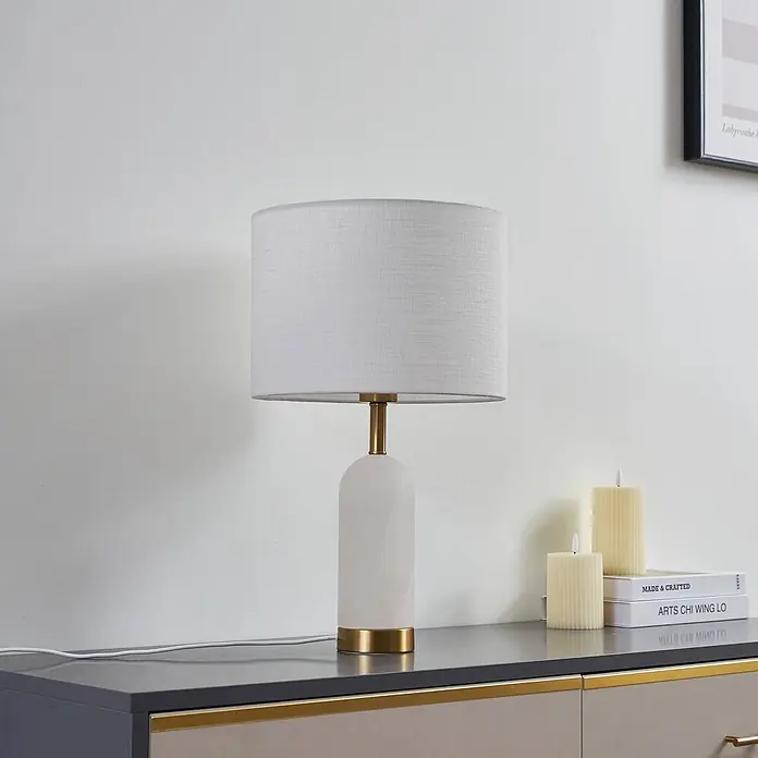 Lindby Tischleuchte Alabaster - alu / grau / zink, weiß / opal, E27 - Weiße Tischlampe mit Stoffschirm, weißem Marmorfuß und goldenen Akzenten, auf einer Konsole platziert.