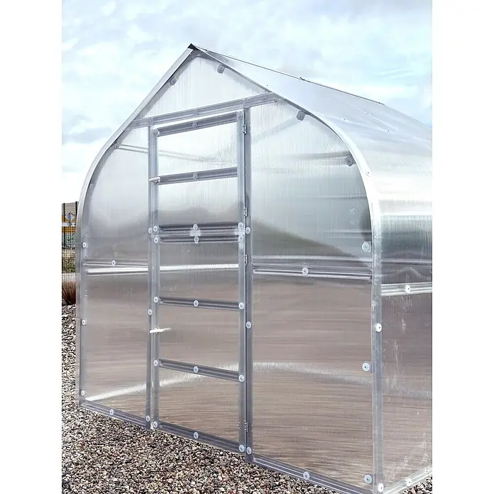 Klasika Greenhouses Gewächshaus Drop Klasika - Außenmaß inkl. Dachüberstand (B x T): 250 x 1.200 cm, Material Seitenwand: Kunststoff, 6 mm, Silbergrau - Ein lichtdurchlässiges Polycarbonat-Gewächshaus mit Metallrahmen, auf Kies unter einem bewölkten Himmel.