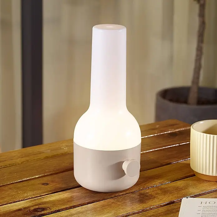 Lindby Tischleuchte Isaline - creme / amber, creme / amber - Beleuchtete moderne Tischlampe mit weißem mattiertem Diffusor und hellbeigem Sockel auf einem Holztisch.