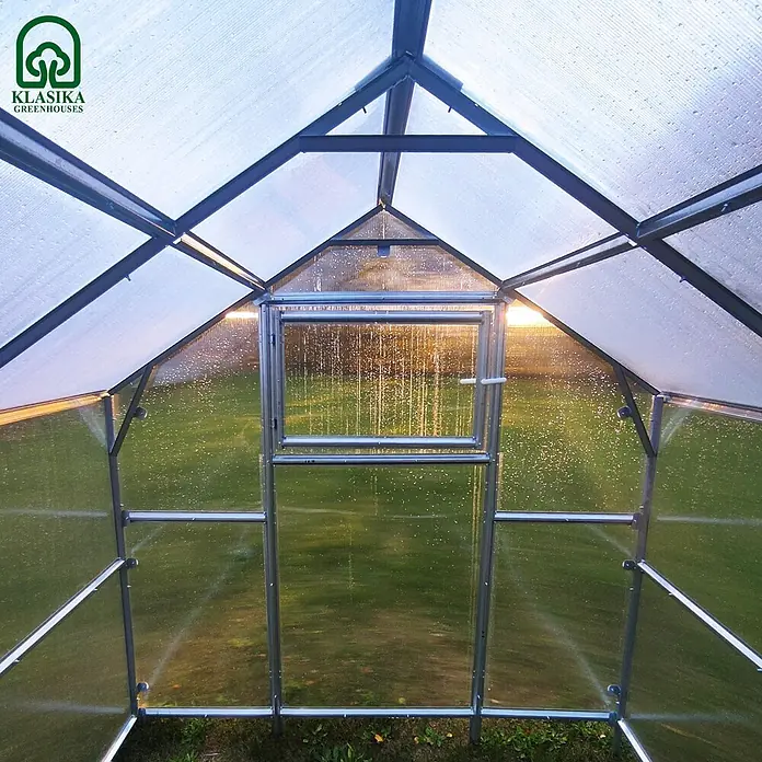 Klasika Greenhouses Gewächshaus Bernard Klasika - Außenmaß inkl. Dachüberstand (B x T): 235 x 500 cm, Material Seitenwand: Kunststoff, 6 mm, Silbergrau - Innenansicht eines Klasika Gewächshauses mit transparenten, gewellten Platten, robustem Metallrahmen und Sonnenlicht auf Wassertropfen.