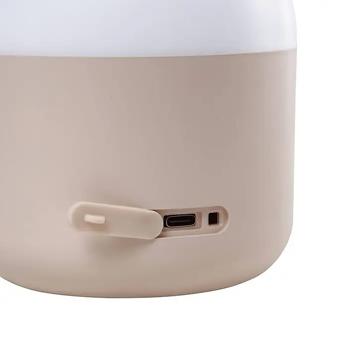 Lindby Tischleuchte Isaline - creme / amber, creme / amber - Hellbeiges Gerät mit weißer Oberseite, zeigt eine teilweise geöffnete Schutzklappe über einem USB-C-Ladeanschluss und eine kleine Anzeigeleuchte.