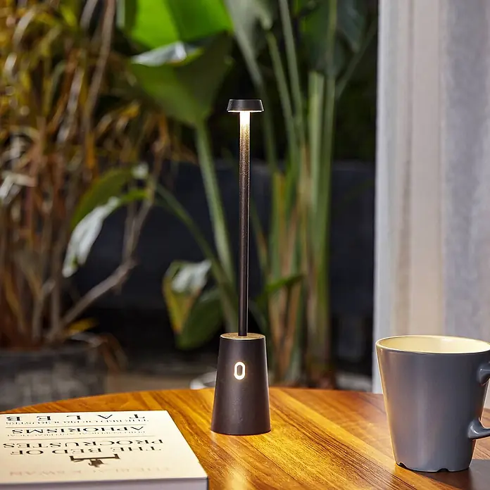 Lindby Tischleuchte Noelani - L x B x H: 5,5 x 5,5 x 30 cm, schwarz, schwarz - Hohe, schlanke schwarze Metall-Tischleuchte auf Holztisch, spendet warmes Licht, mit beleuchteter '0' am Fuß.