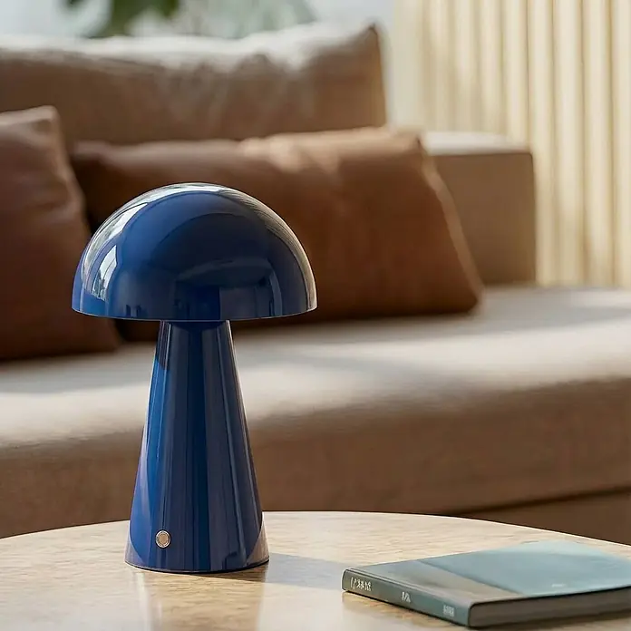 Lindby Tischleuchte Nevijo - L x B x H: 20 x 20 x 30 cm, blau, blau - Glänzende blaue Pilztischlampe auf hellem Tisch, schafft gemütliche Wohnzimmeratmosphäre. Ein Buch liegt daneben.
