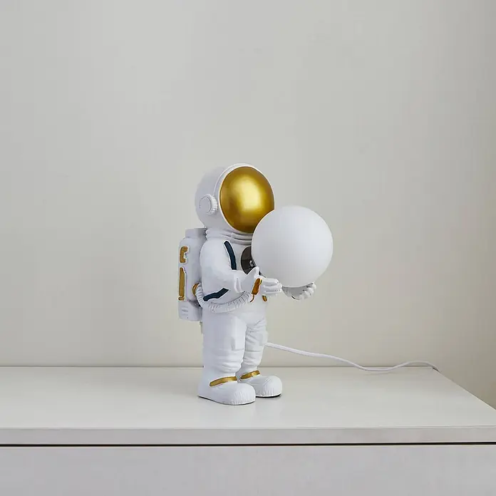 Lindby Tischleuchte Kosmo - L x B x H: 22,5 x 14 x 31 cm, weiß / opal, weiß / opal, G9 - Weiße Astronautenlampe mit goldfarbenem Visier und Details, die ein kugelförmiges weißes Licht hält.