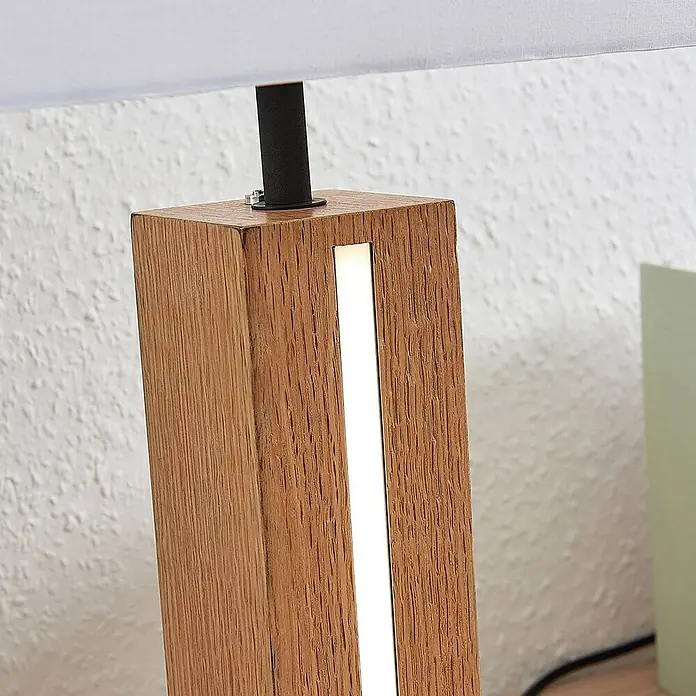 Lindby Tischleuchte Garry - L x B x H: 32 x 20 x 52,5 cm, Holz hell, weiß / opal, E27 - Nahaufnahme einer modernen Tischlampe mit Naturholzsockel, integriertem vertikalen LED-Streifen und hellem Stoffschirm.