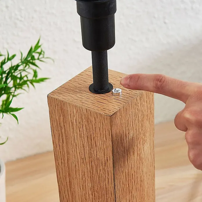 Lindby Tischleuchte Garry - L x B x H: 32 x 20 x 52,5 cm, Holz hell, weiß / opal, E27 - Ein Finger drückt einen silbernen Knopf auf einem hellen Holzblock mit einem schwarzen Metallstab, möglicherweise ein Lampenfuß.