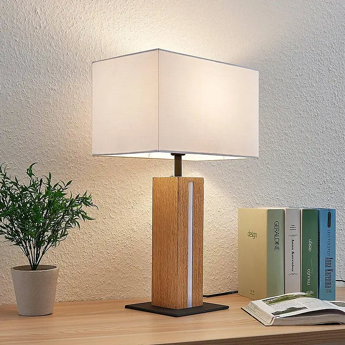 Lindby Tischleuchte Garry - L x B x H: 32 x 20 x 52,5 cm, Holz hell, weiß / opal, E27 - Eine Tischlampe mit rechteckigem weißem Schirm und Holzfuß mit vertikalem Lichtstreifen, auf einem Holztisch.