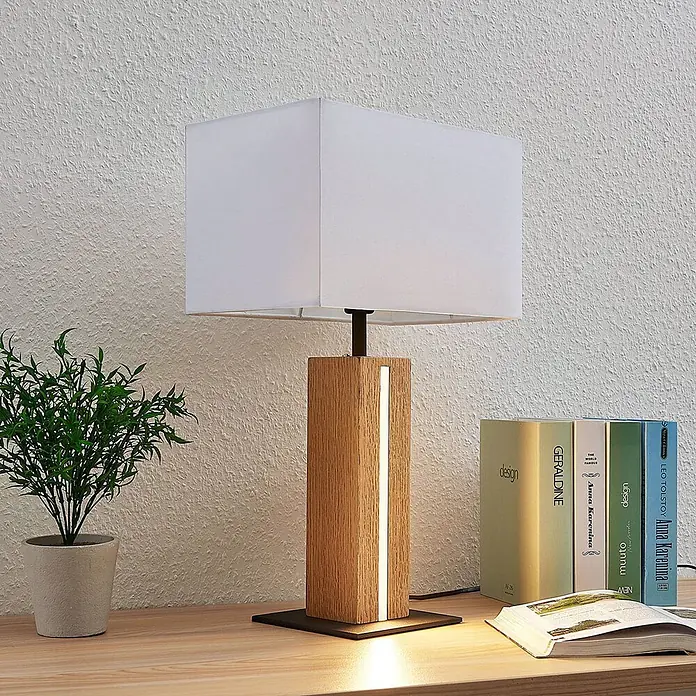 Lindby Tischleuchte Garry - L x B x H: 32 x 20 x 52,5 cm, Holz hell, weiß / opal, E27 - Eine moderne Tischlampe mit hellem Holzsockel, integriertem LED-Streifen und rechteckigem weißen Stoffschirm, steht auf einem Holzschreibtisch.