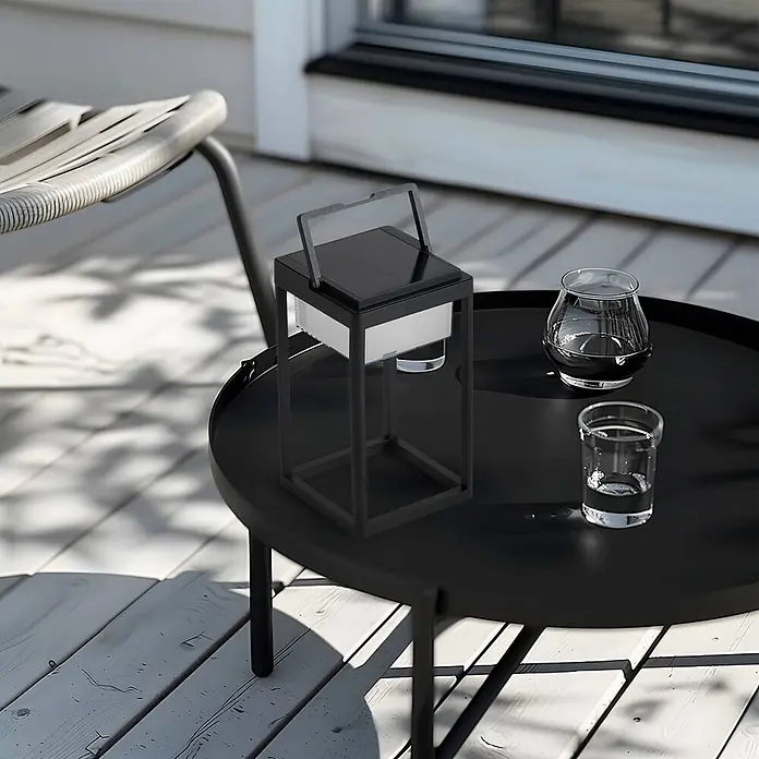 Lucande Tischleuchte Tilena - L x B x H: 18,5 x 18,5 x 32 cm, schwarz - Eine schwarze Solar-Laterne mit Griff steht auf einem Beistelltisch im Freien, bereit zur Beleuchtung.