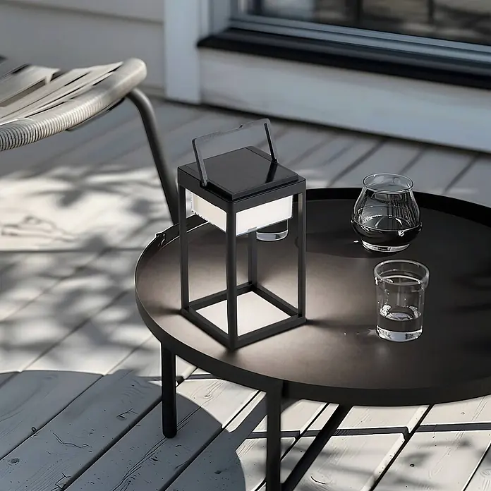 Lucande Tischleuchte Tilena - L x B x H: 18,5 x 18,5 x 32 cm, schwarz - Moderne schwarze Solarlaterne mit Griff und weißem Licht, auf einem dunklen Gartentisch neben Gläsern.