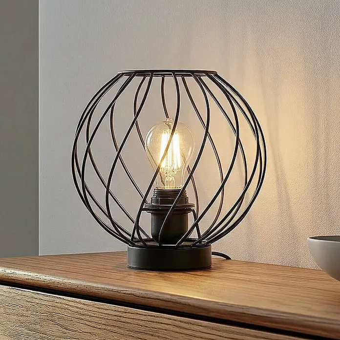 Lindby Tischleuchte Danika - schwarz, E27 - Tischleuchte mit schwarzem Drahtkäfig und sichtbarer Edison-LED-Birne auf einer Holzkommode.