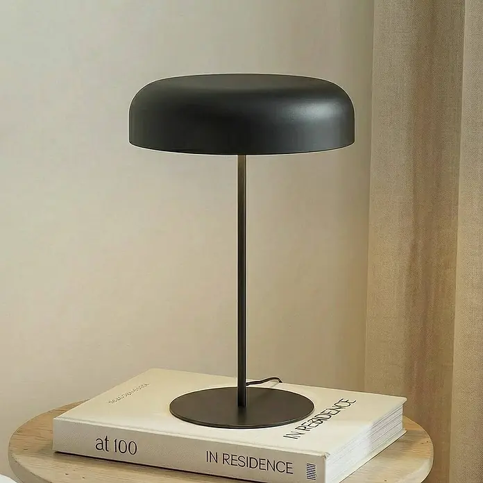 Lindby Tischleuchte Edion - schwarz, schwarz, E14 - Moderne schwarze Tischleuchte mit Kuppelschirm und dünnem Stiel, auf einem Buch auf einem Holztisch.