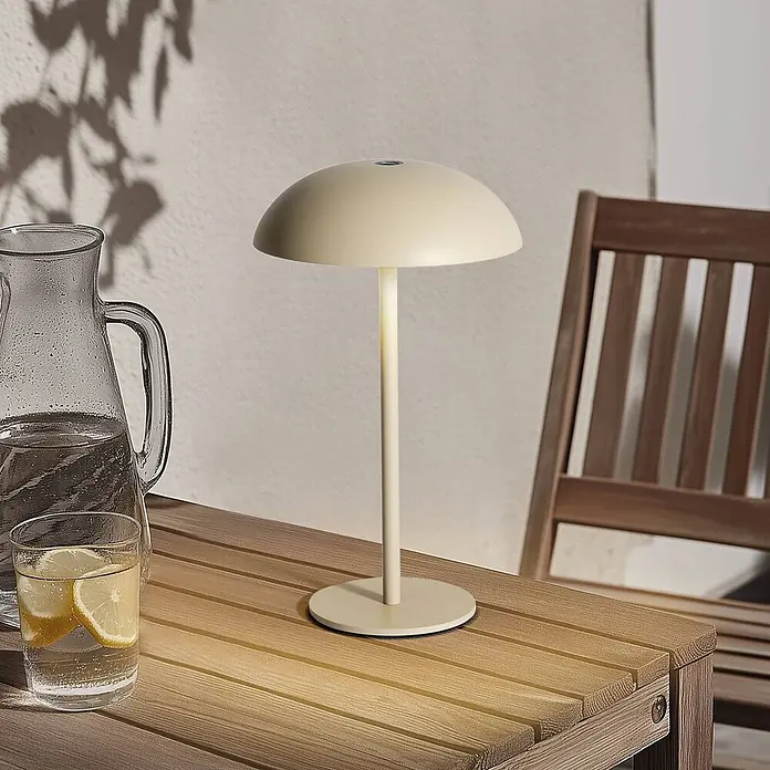 Arcchio Tischleuchte Thenra - L x B x H: 15,4 x 15,4 x 9,5 cm, creme / amber, creme / amber - Cremefarbene tragbare Tischlampe mit pilzförmigem Schirm, beleuchtet einen Holztisch im Freien mit Getränken.