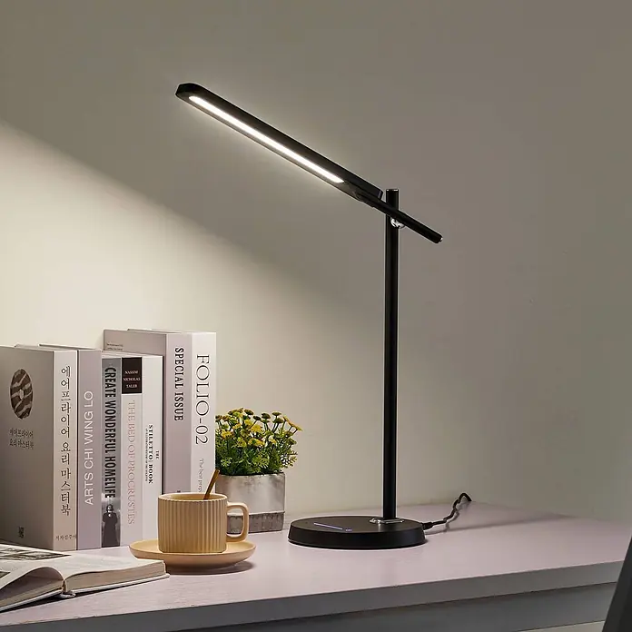 Lindby Tischleuchte Valtorin - L x B x H: 41,8 x 17,8 x 45,7 cm, schwarz, schwarz - Eine schlanke, schwarze LED-Schreibtischlampe beleuchtet einen Schreibtisch mit Büchern und Tasse. Ihr verstellbarer Arm trägt eine lineare Lichtquelle.