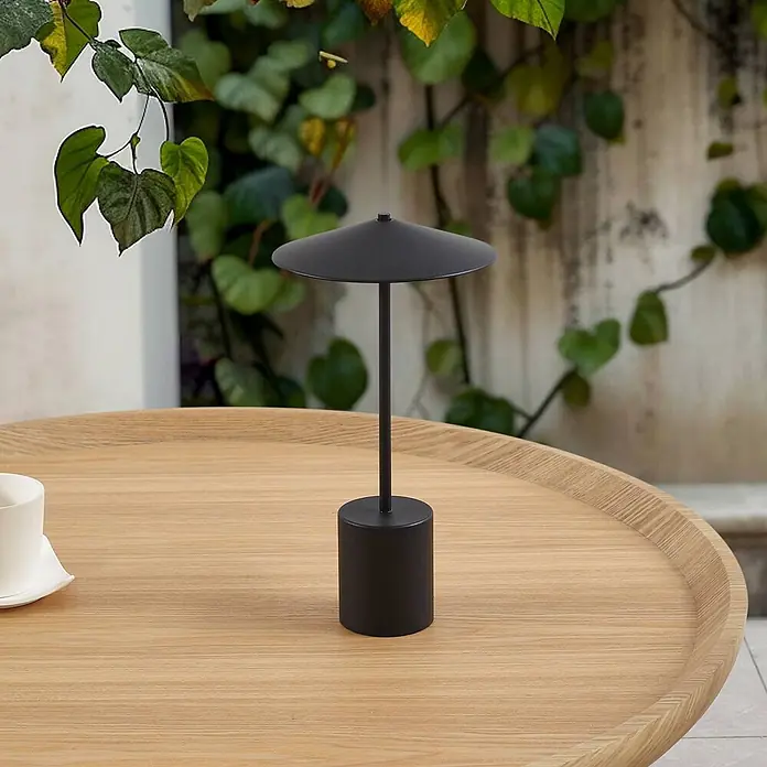 Lindby Tischleuchte Ayva - schwarz, schwarz - Elegante schwarze tragbare Tischleuchte auf einem hellen Holztisch im Freien.