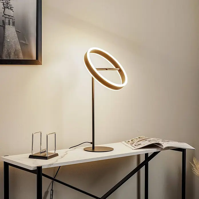 Lucande Tischleuchte Yekta - L x B x H: 30 x 30 x 58,5 cm, schwarz, schwarz - Moderne runde LED-Tischlampe mit goldfarbenem Ring und dunklem Standfuß, beleuchtet einen weißen Marmortisch.