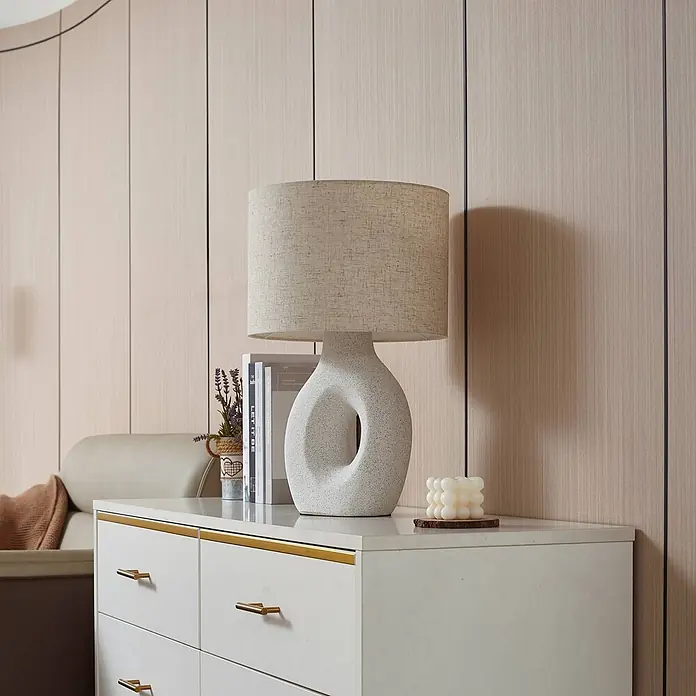 Lindby Tischleuchte Thalassia - weiß / opal, weiß / opal, E27 - Eine moderne Tischlampe mit hellem Textilstoffschirm und skulpturalem gesprenkeltem Keramikfuß auf einer weißen Kommode.
