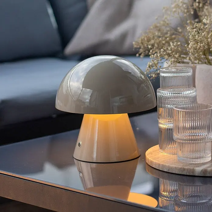 Lindby Tischleuchte Nevijo - alu / grau / zink, alu / grau / zink - Glänzende taupe Pilztischlampe spendet warmes Licht auf einer reflektierenden Oberfläche.