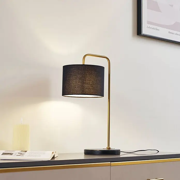 Lindby Tischleuchte Hillary - schwarz, schwarz, E27 - Elegante Tischlampe mit schwarzem Stoffschirm und goldfarbenem Metallgestell, die warmes Licht auf einen Konsolentisch wirft.