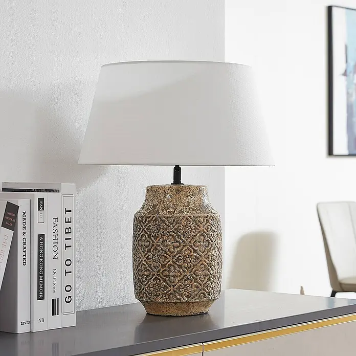 Lindby Tischleuchte Aelith - L x B x H: 40 x 40 x 49 cm, alu / grau / zink, weiß / opal, E27 - Stehlampe mit weißem Schirm und strukturierter Keramikbasis auf einer Konsole neben Büchern.