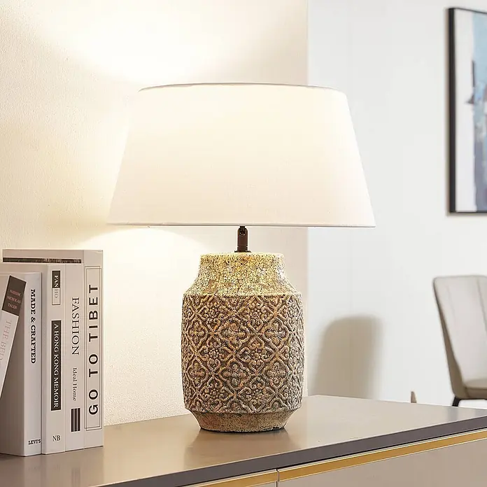 Lindby Tischleuchte Aelith - L x B x H: 40 x 40 x 49 cm, alu / grau / zink, weiß / opal, E27 - Eine strukturierte, gemusterte Tischlampe mit weißem Schirm beleuchtet einen Raum auf einem Konsolentisch.