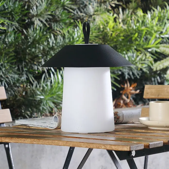 Lindby Tischleuchte Kalina - schwarz - Tragbare Outdoor-Tischlampe mit mattweißem Fuß, schwarzem konischem Schirm und schwarzem Griff, auf einem Holztisch stehend.