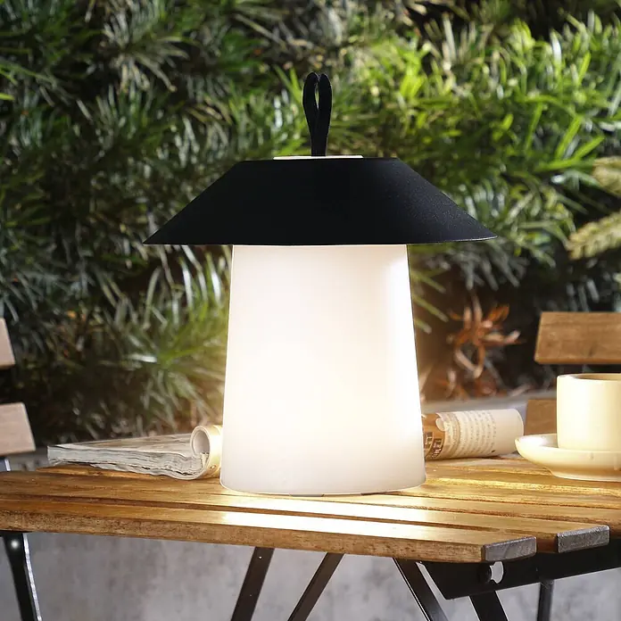 Lindby Tischleuchte Kalina - schwarz - Moderne schwarz-weiße tragbare Tischlampe mit leuchtendem Sockel auf einem Holztisch.