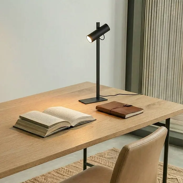 Lucande Tischleuchte Lysias - schwarz, schwarz, GU10 - Elegante schwarze Schreibtischlampe aus Metall beleuchtet ein offenes Buch auf einem hellen Holztisch, daneben ein braunes Notizbuch.