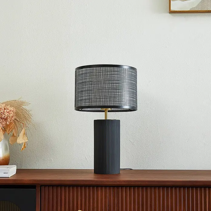 Lindby Tischleuchte Sorscha - schwarz, schwarz, E27 - Schwarze Tischlampe mit gerilltem Sockel und Gitterschirm auf einer Holzkommode.