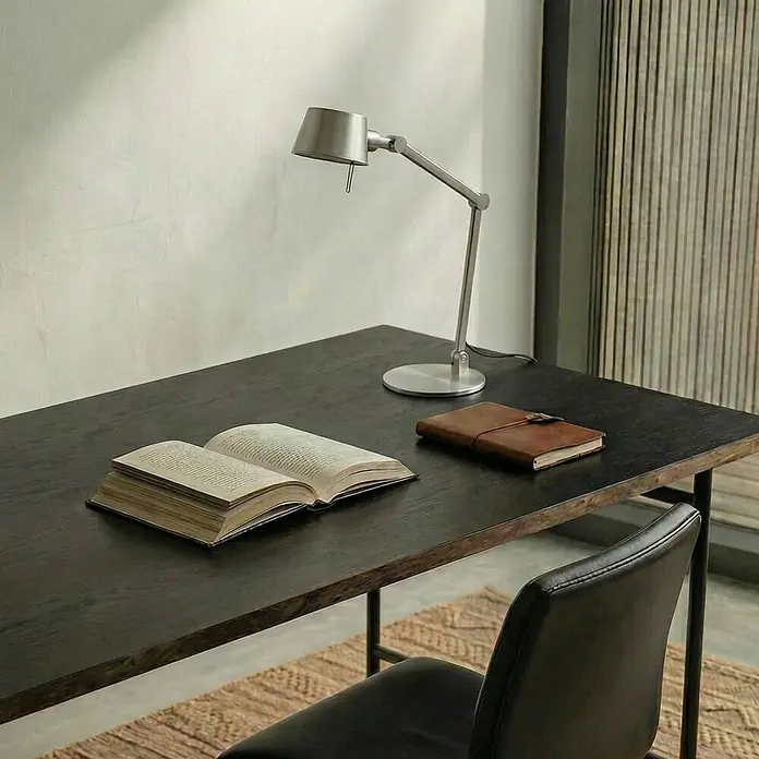 Lucande Tischleuchte Silka - alu / grau / zink, alu / grau / zink, E27 - Eine verstellbare silberne Schreibtischlampe, ein offenes Buch und ein braunes Ledernotizbuch liegen auf einem dunklen Holzschreibtisch. Ein schwarzer Stuhl ist teilweise sichtbar.