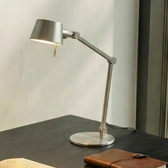 Lucande Tischleuchte Silka - alu / grau / zink, alu / grau / zink, E27 - Moderne silberne Schreibtischlampe mit verstellbarem Arm auf dunklem Holzschreibtisch, beleuchtet einen Arbeitsbereich.