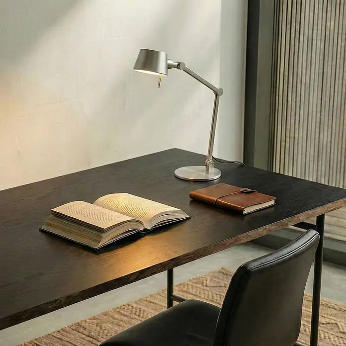 Lucande Tischleuchte Silka - alu / grau / zink, alu / grau / zink, E27 - Silberne verstellbare Schreibtischlampe beleuchtet ein offenes Buch auf einem dunklen Holzschreibtisch.