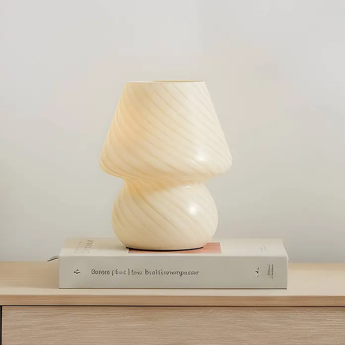 Lindby Tischleuchte Andriana - gelb / orange, gelb / orange, E14 - Pilz-Tischlampe aus gewirbeltem, opaquem cremefarbenem Glas, auf einem Buch stehend.