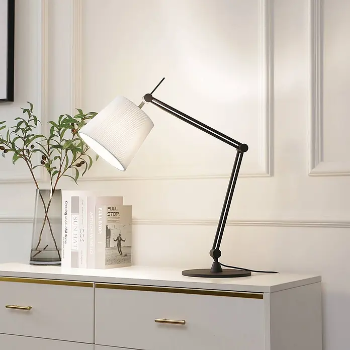 Lucande Tischleuchte Caelia - L x B x H: 22 x 69 x 64,5 cm, schwarz, weiß / opal, E27 - Schwarze, verstellbare Schreibtischlampe mit weißem Faltschirm, beleuchtet eine Kommode mit Büchern und Pflanze.