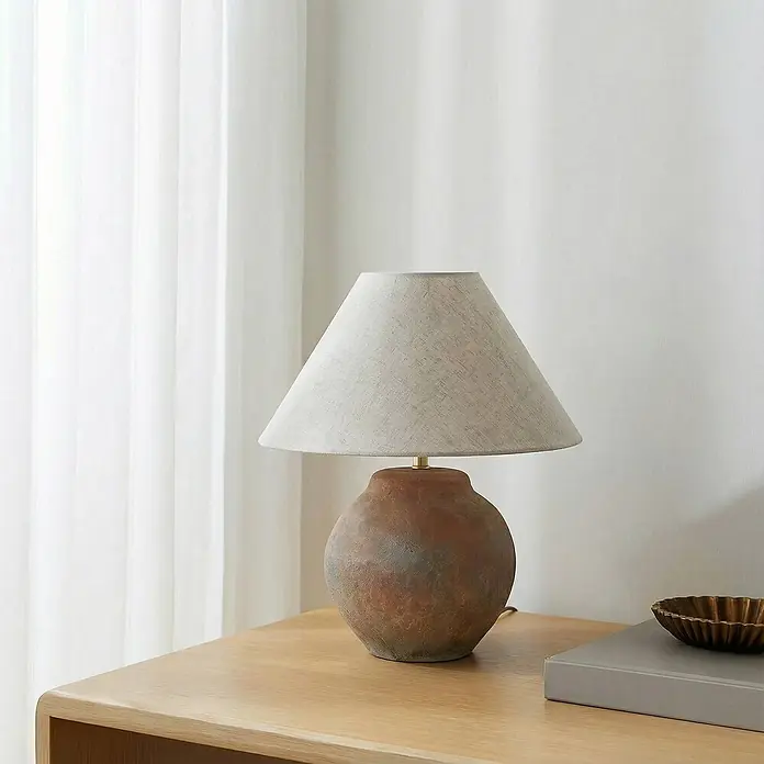 Lucande Tischleuchte Thalorin - braun / rost, E27 - Tischlampe in Terrakotta-Optik mit strukturierter, runder Basis und hellem Stoffschirm, auf einem hellen Holztisch.