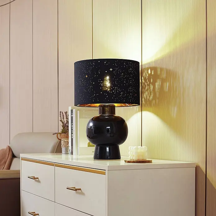 Lindby Tischleuchte Arved - L x B x H: 30 x 30 x 46 cm, schwarz, schwarz, E27 - Schwarze Tischlampe mit glänzendem Fuß und schwarzem Lampenschirm mit Sternausschnitten, beleuchtet und Sterne an die Wand werfend.