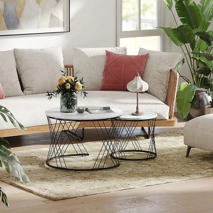 Couchtisch Set -  - Zwei Beistelltische mit weißen Marmorplatten und schwarzen Drahtgestellen in einem Wohnzimmer. Einer trägt Blumen und einem Magazin, der andere eine Lampe.