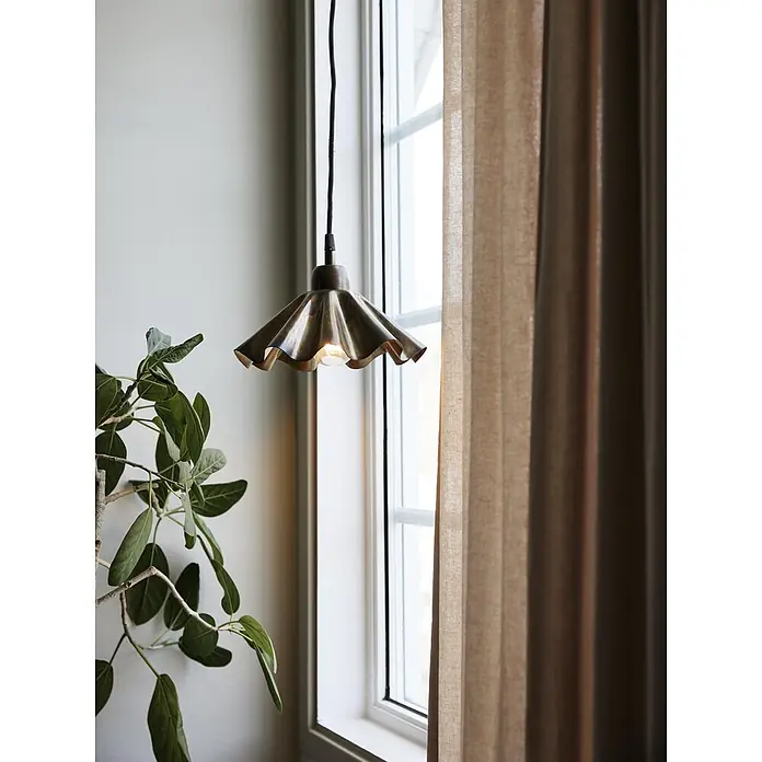 PR Home Pendelleuchte Aira - 240 W, E27 - Eine messingfarbene Pendelleuchte mit Rüschen hängt beleuchtet in einem Fensterambiente mit einer Pflanze und einem Vorhang.