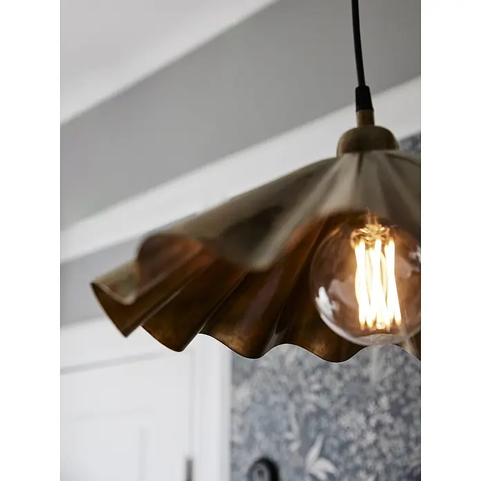 PR Home Pendelleuchte Aira - 40 W, E27 - Nahaufnahme einer geriffelten Messing-Pendelleuchte mit leuchtender Edison-LED-Birne, hängend in einem Innenraum.