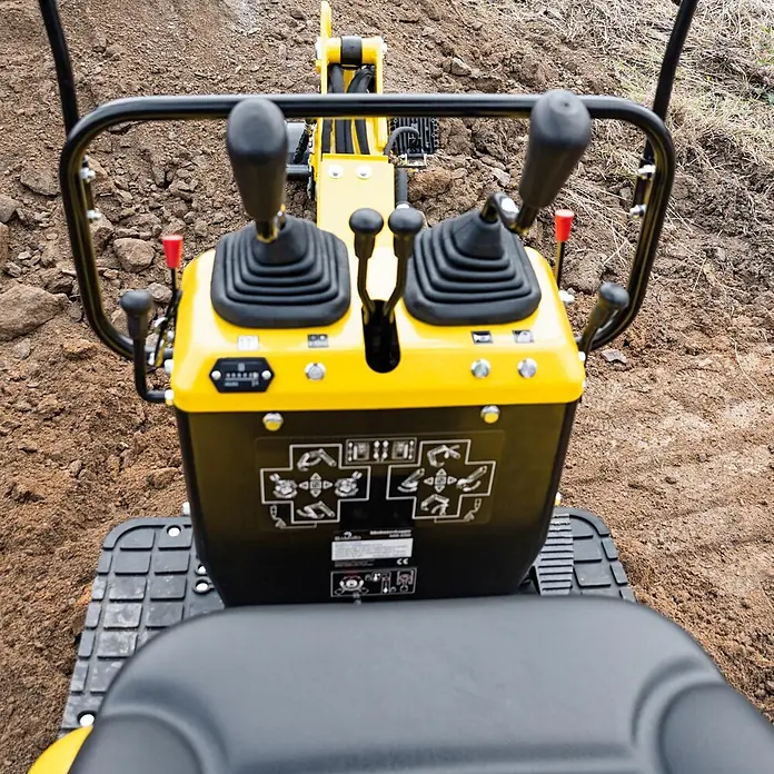 Bamato Minibagger MIB-600 - 6.300 W, Benzin, Auslegerschwenkbereich: 70 ° - Gelbes und schwarzes Bedienfeld eines Minibaggers mit Joysticks und Gummikette in lockerer Erde.