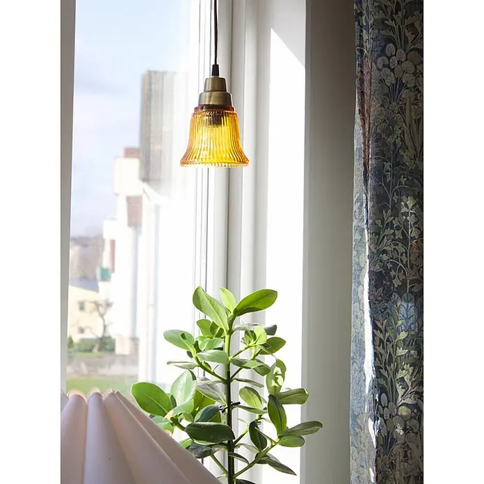 PR Home Pendelleuchte Fensterleuchte - 25 W, E27 - Kleine gelbe gerippte Glaspendelleuchte mit Messing in einem hellen Fenster neben einer grünen Pflanze und einem gemusterten Vorhang.