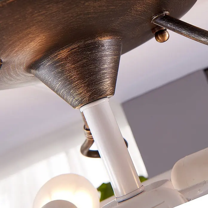 Lindby Deckenleuchte Rando - alu / grau / zink, E27 - Nahaufnahme einer Deckenleuchte mit patiniertem Bronzefuß, einem weißen Metallarm und einer leuchtenden satinierten Glühbirne.